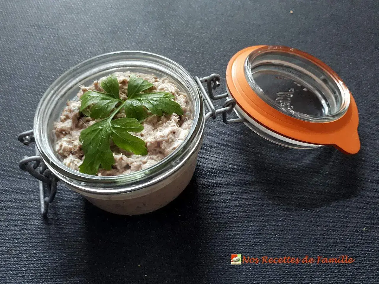 Un bocal ouvert révèle de délicieuses rillettes de sardines, garnies d'une feuille de persil frais.