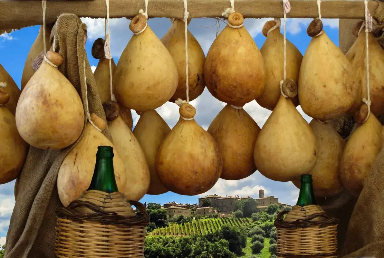 Formaggio cacio appeso, con sfondo di un borgo toscano e vigneti.