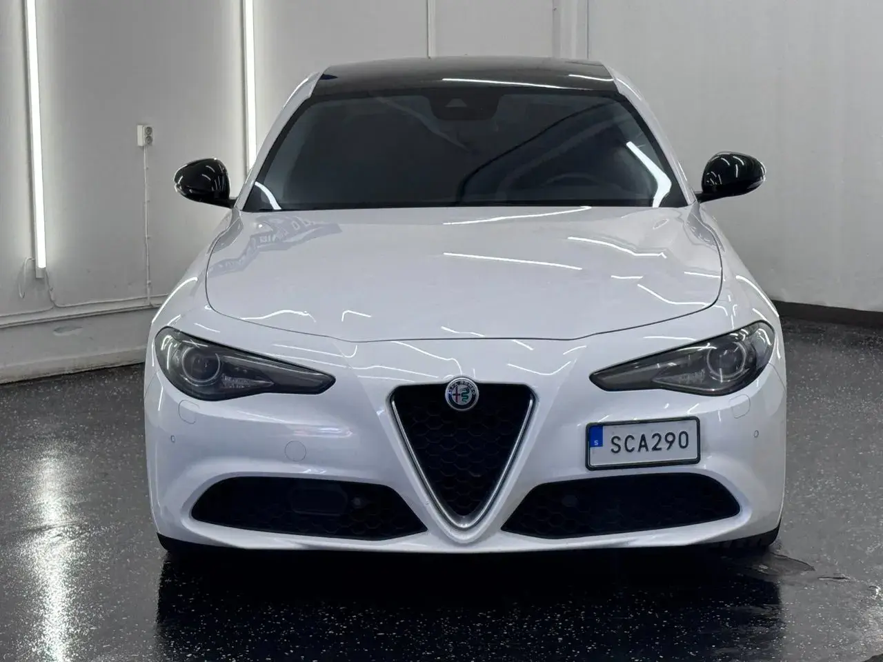 Vit Alfa Romeo Giulia, en elegant begagnad bil med mörk tak och svarta backspeglar. Perfekt för dig som söker stil och prestanda.