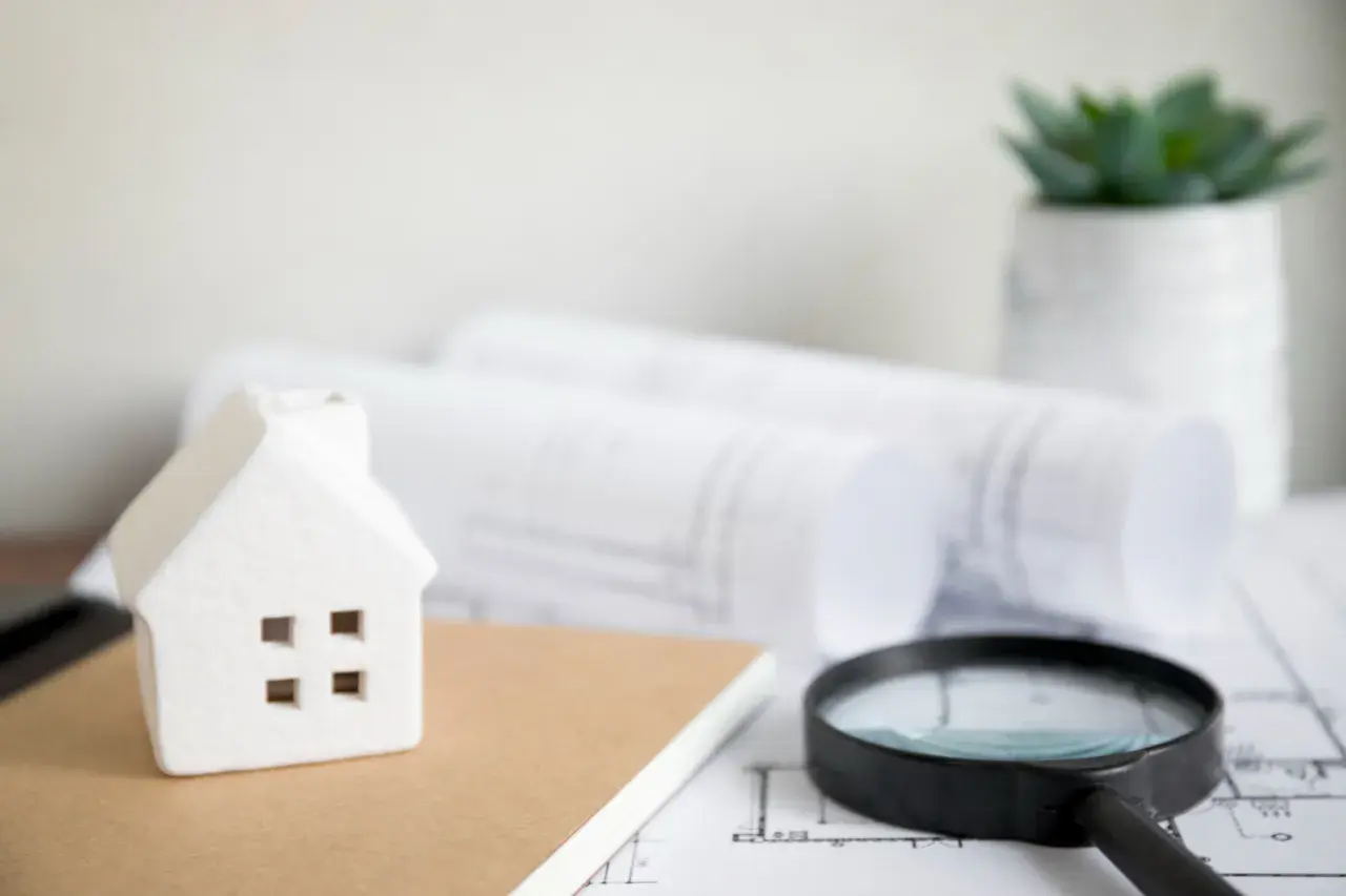 Modellino di casa, lente d'ingrandimento e progetti su un tavolo, pronti per un controllo edilizio.