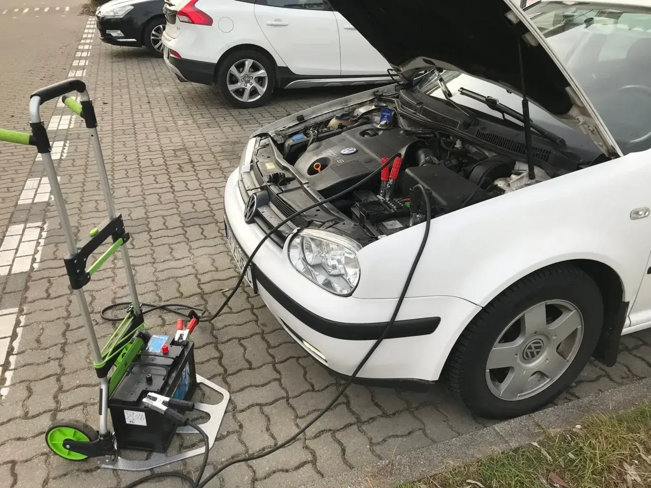 Awaryjny rozruch samochodu: podłączony wózek z akumulatorem do białego VW.