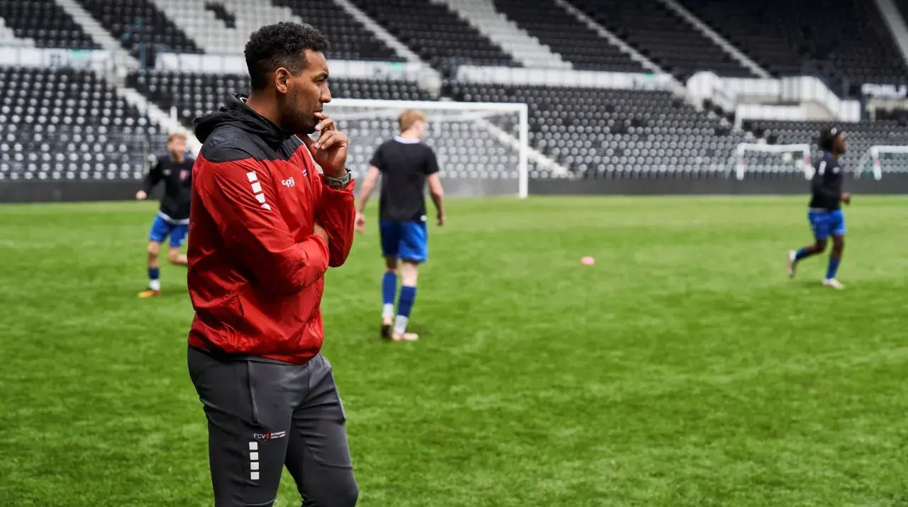 Ein Mann in Rot und Schwarz beobachtet aufmerksam junge Fußballer auf dem Trainingsplatz. Ein typischer Tag im Leben eines Fußball Scout.