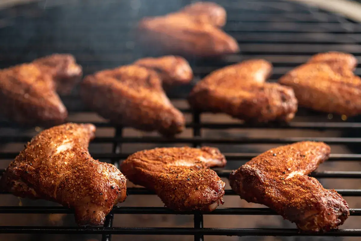 Ailes de poulet marinées pour barbecue, grillées à la perfection, dégageant une fumée alléchante.