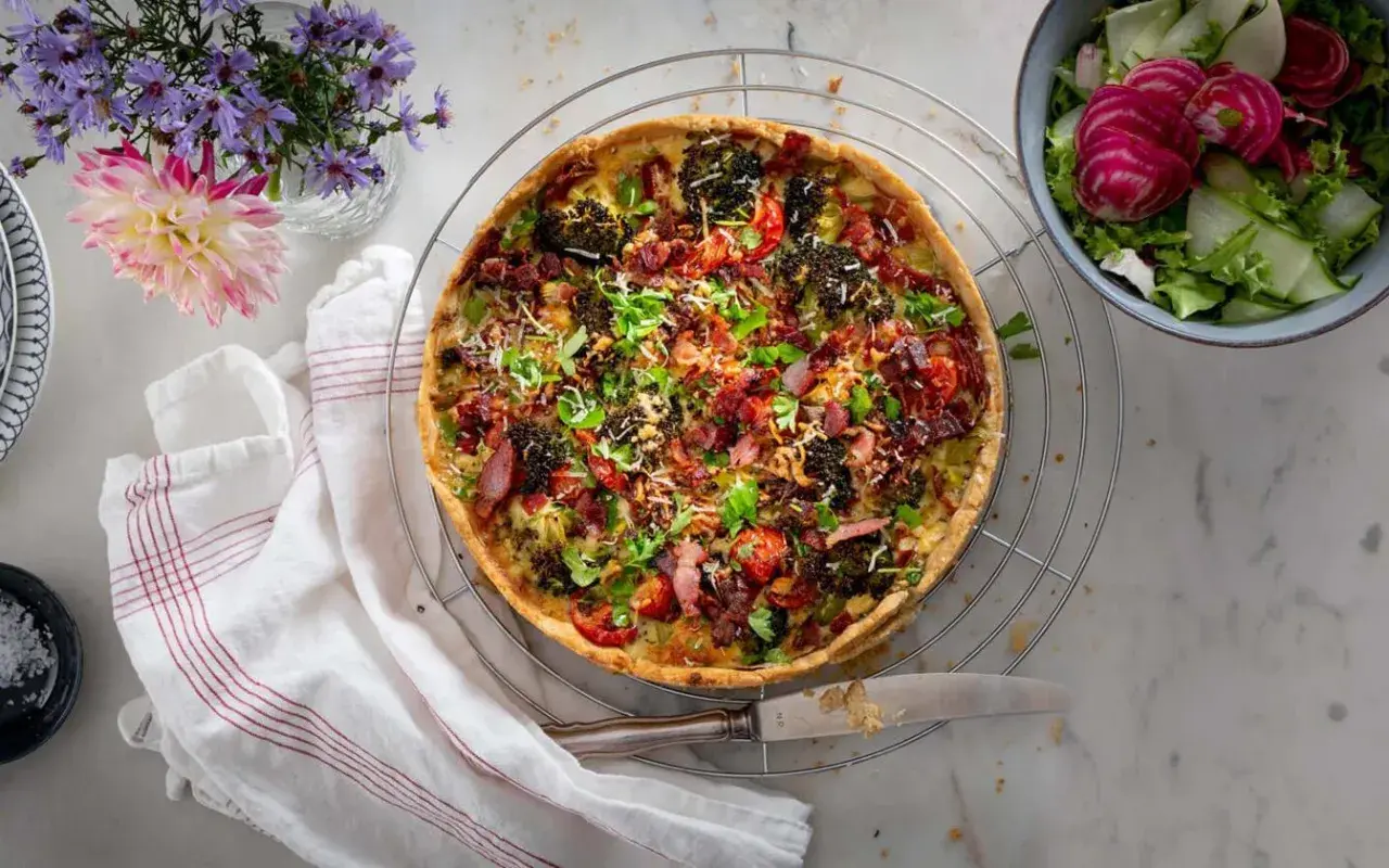 En gyllene quiche lorraine med broccoli, bacon och tomater, serverad med en fräsch sallad.