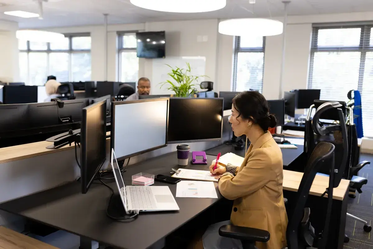 Une femme travaille à son bureau, entourée d'écrans. L'espace de travail semble bien organisé, suggérant une bonne gestion de la taille bureau m2.