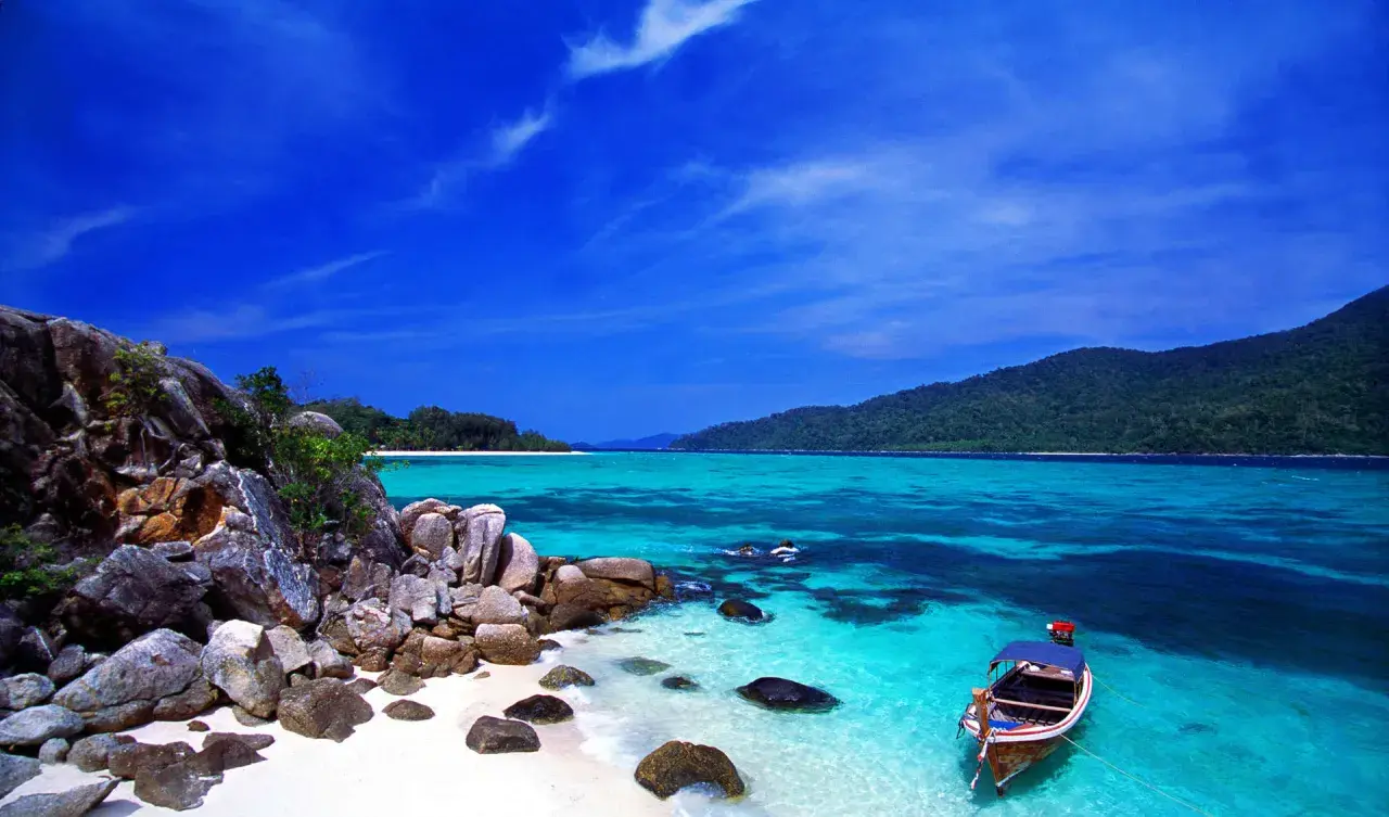 Traumhafte Bucht mit Felsen, weißem Sand und türkisfarbenem Wasser. Ein Boot liegt vor Anker. Perfekt für die beste Reisezeit Thailand.