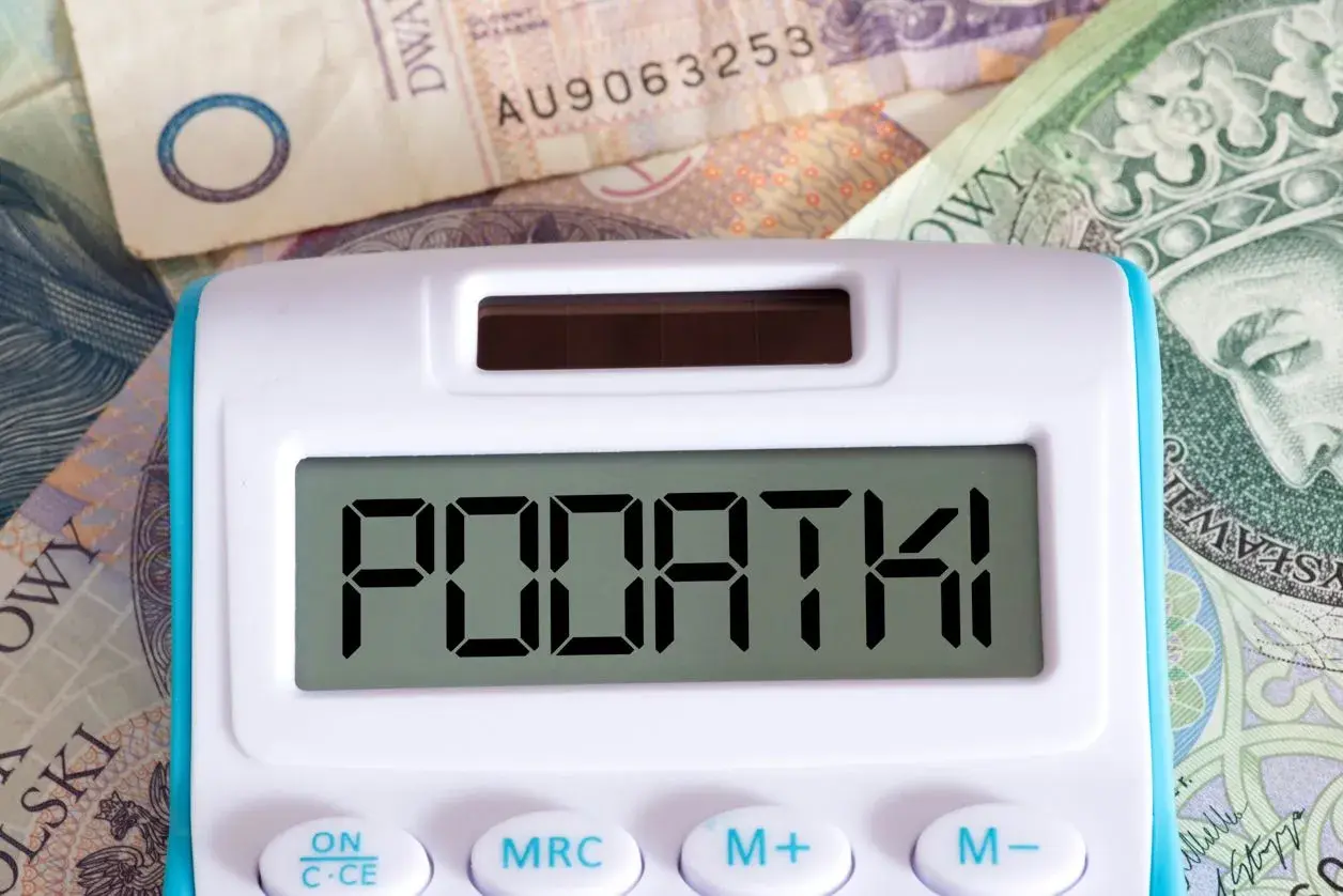 Kalkulator z napisem "PODATKI" na tle polskich banknotów. Czas na rozliczenie PIT 28 druk.
