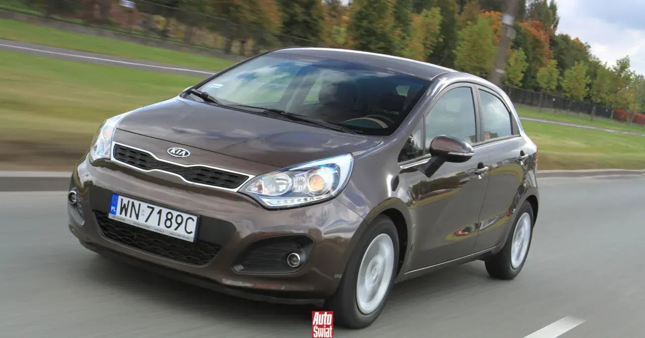 Brązowe Kia Rio 3 w ruchu drogowym, z widocznym grillem i reflektorami.
