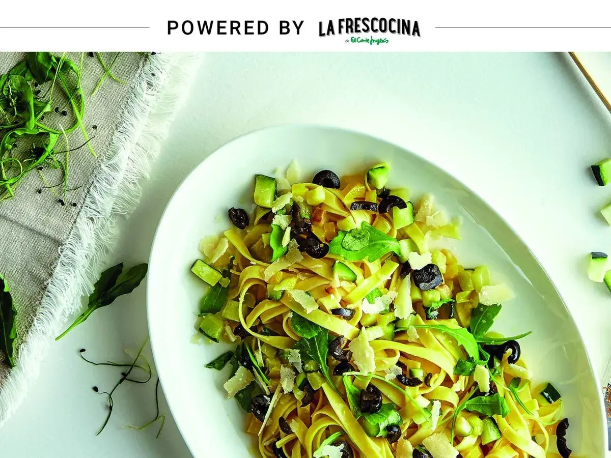 Pasta con verduras frescas, aceitunas negras y queso rallado, servida en un plato blanco.