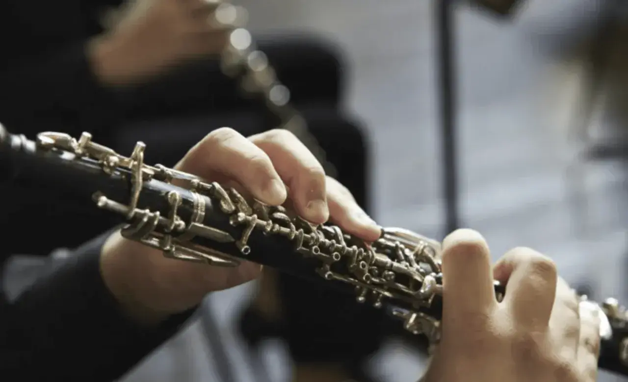 Mains jouant d'un hautbois, un instrument à vent aux clés complexes, évoquant la musique classique.