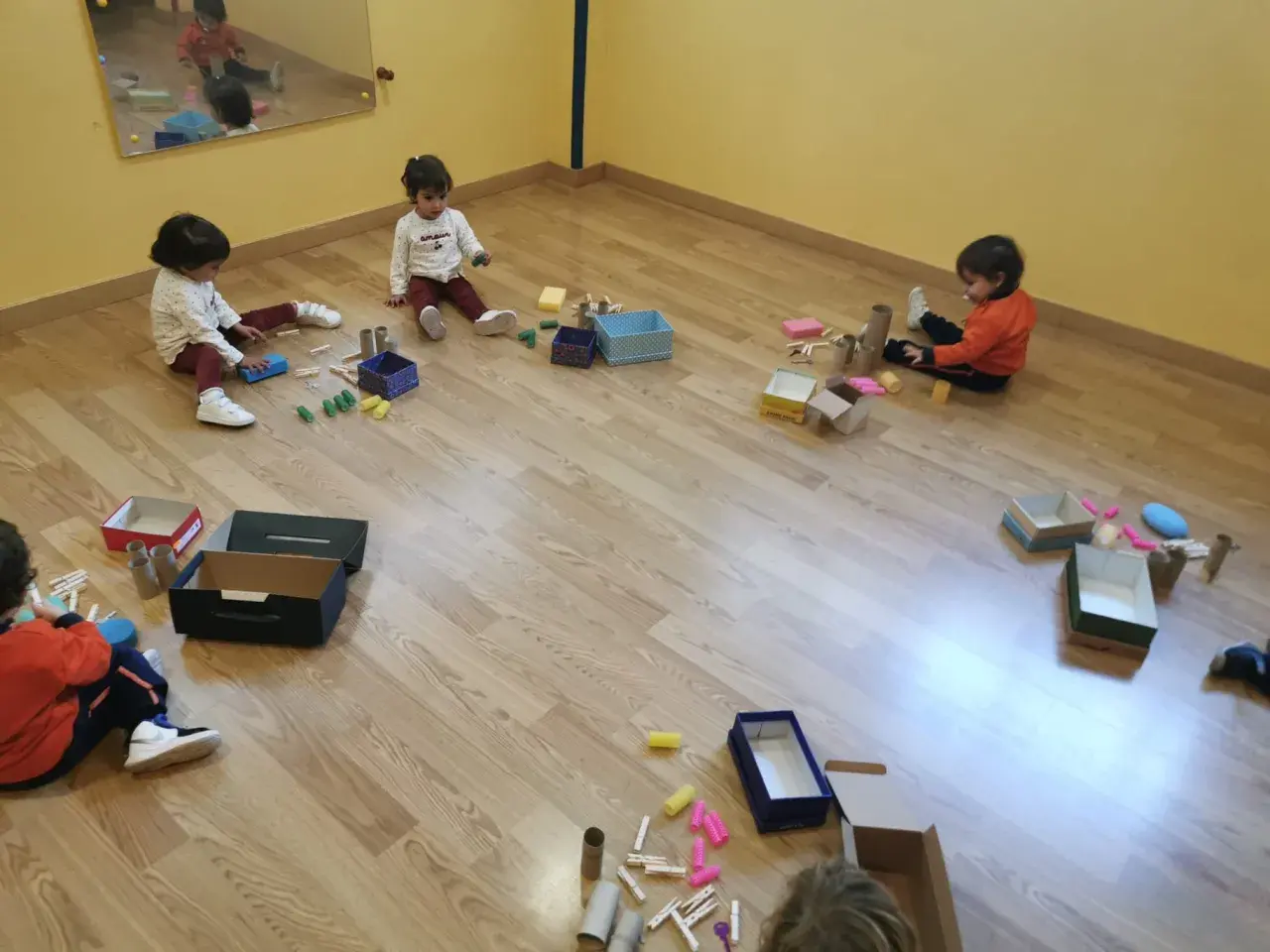 Niños pequeños exploran materiales diversos, cajas y pinzas, aprendiendo sobre el juego heurístico.