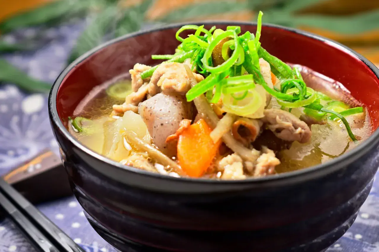 A steaming bowl of tonjiru recipe, filled with pork, vegetables, and topped with fresh green onions.