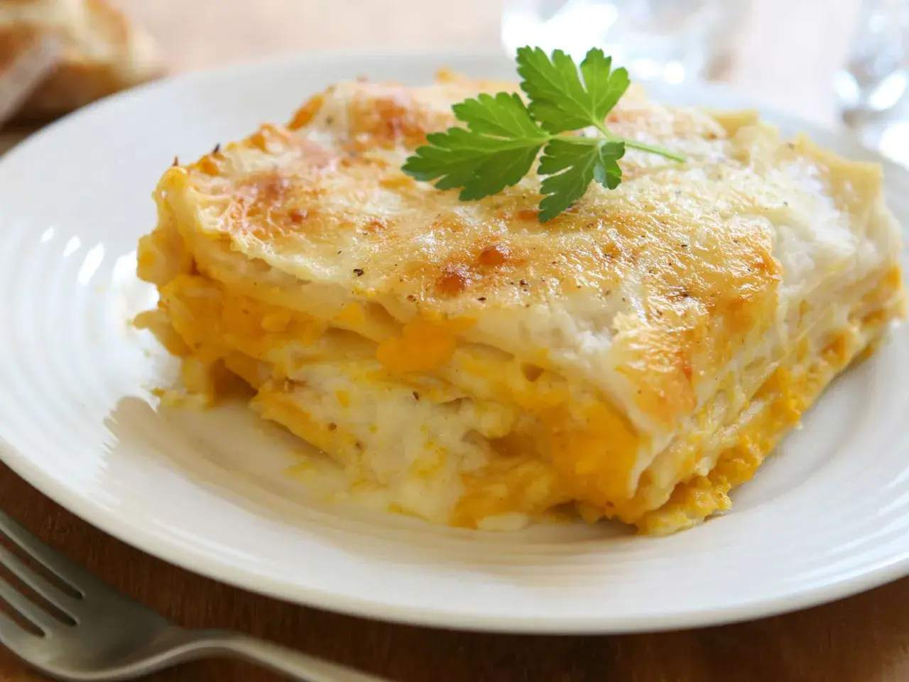 Une part de lasagne de butternut dorée et gratinée, garnie d'une feuille de persil, sur une assiette blanche.