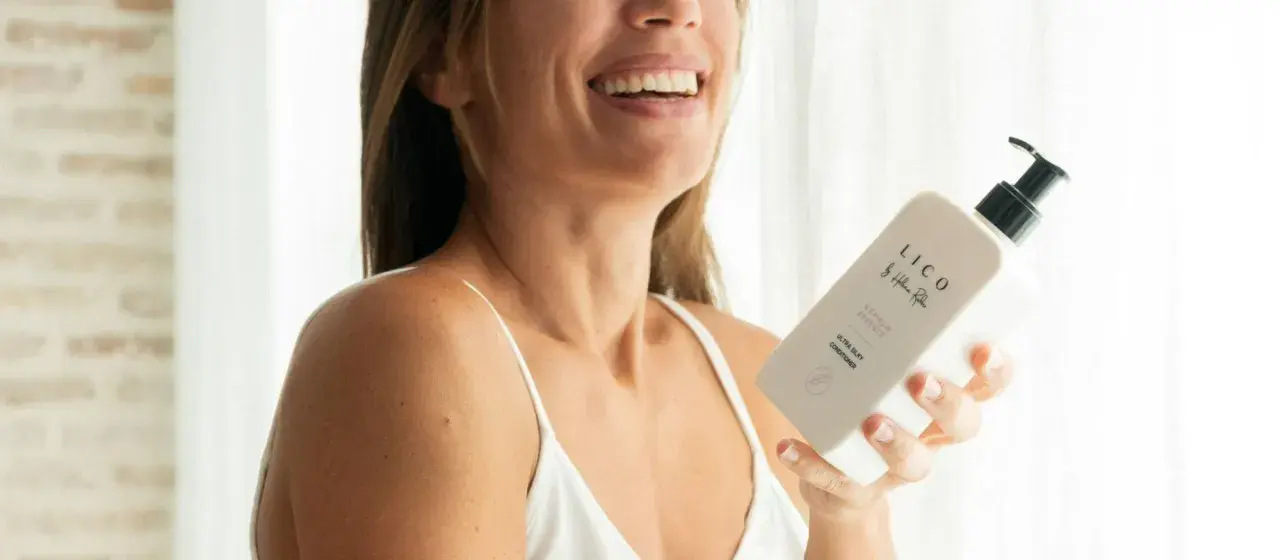 Mujer sonriente sostiene un acondicionador LICO. Descubre para qué sirve el acondicionador del pelo: suavidad y brillo.