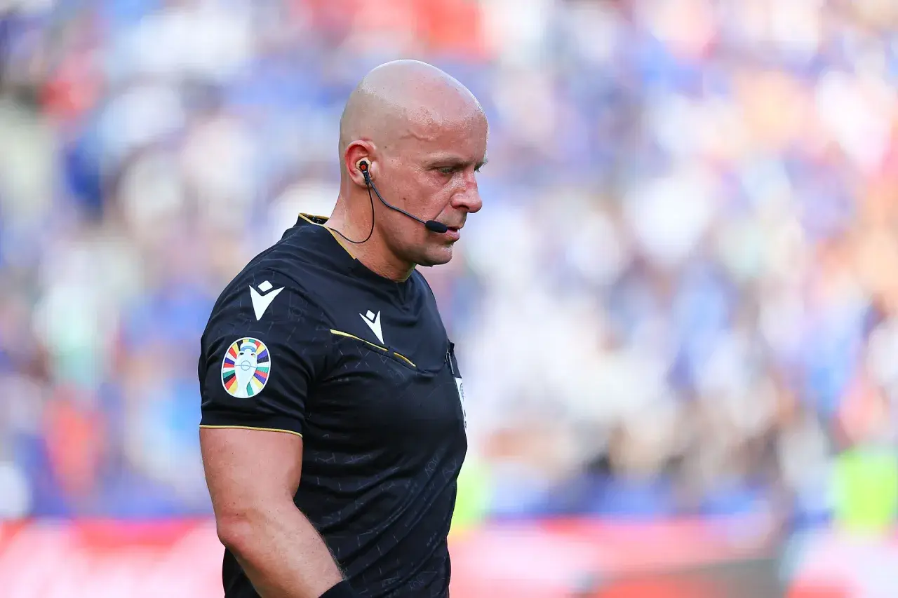 Sędzia Michael Oliver w czarnej koszulce z naszywką Ligi Mistrzów, skupiony na boisku.