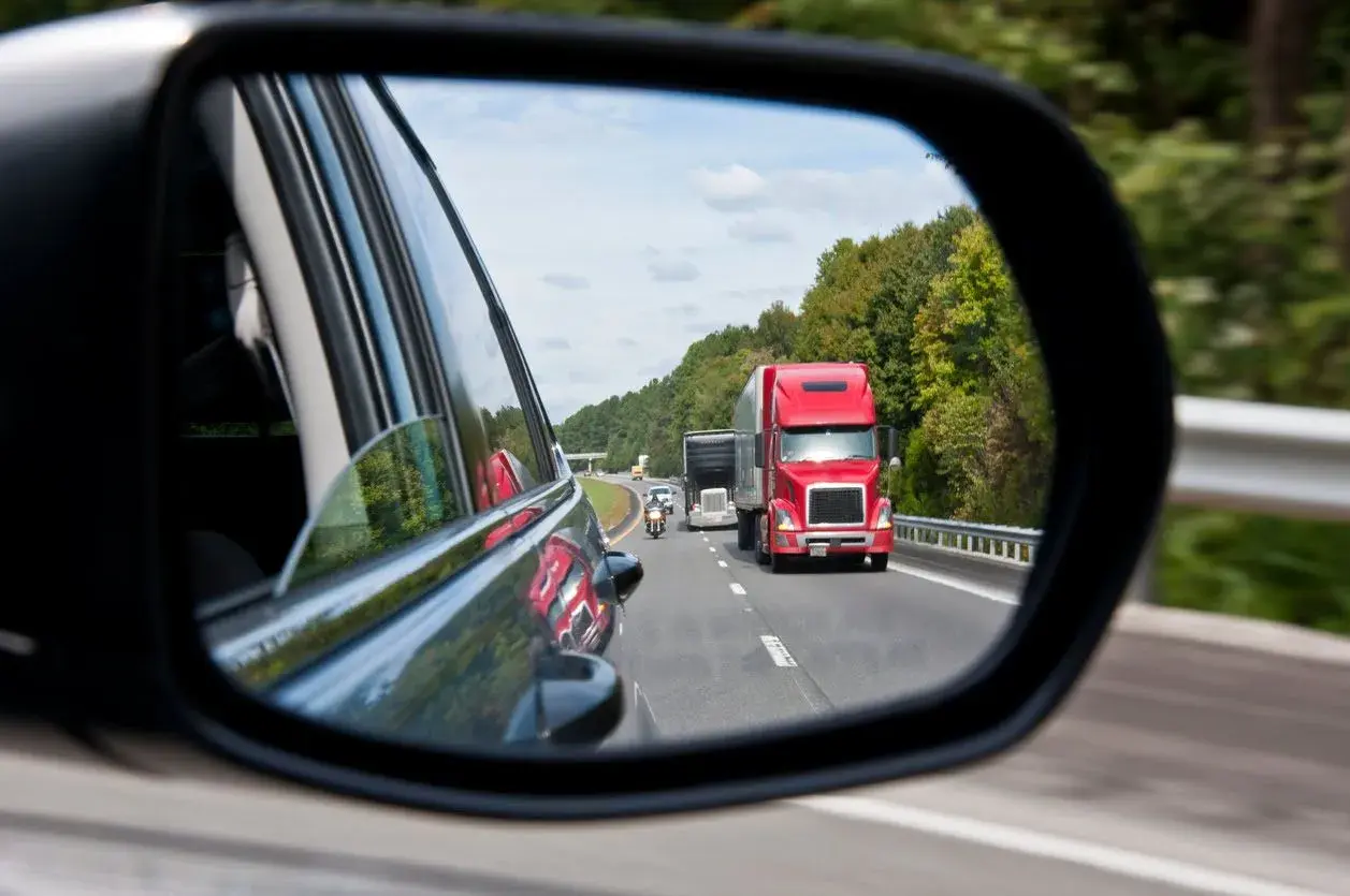 Reflejo en el espejo retrovisor: un camión rojo y una moto circulan por la carretera. ¡Atención! una moto puede adelantar por la derecha.