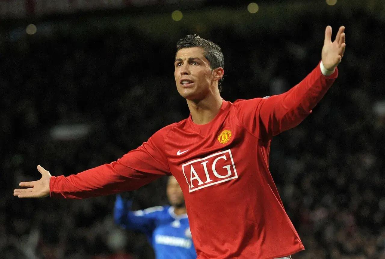Cristiano Ronaldo w czerwonej koszulce Manchesteru United, z uniesionymi rękami, świętuje bramkę. To był kluczowy moment przed jego transferem.