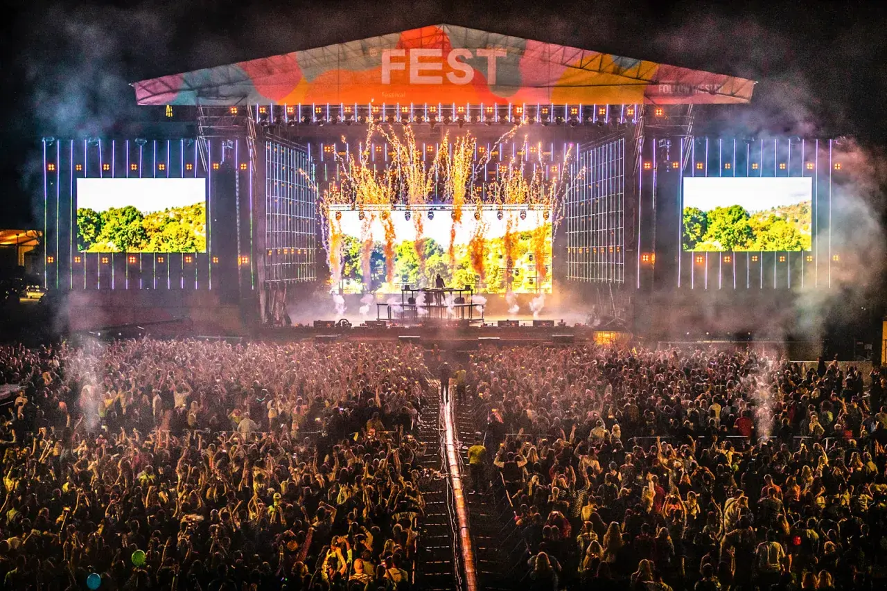 Ogromny tłum na fest festiwalu, scena rozświetlona fajerwerkami i ekranami.