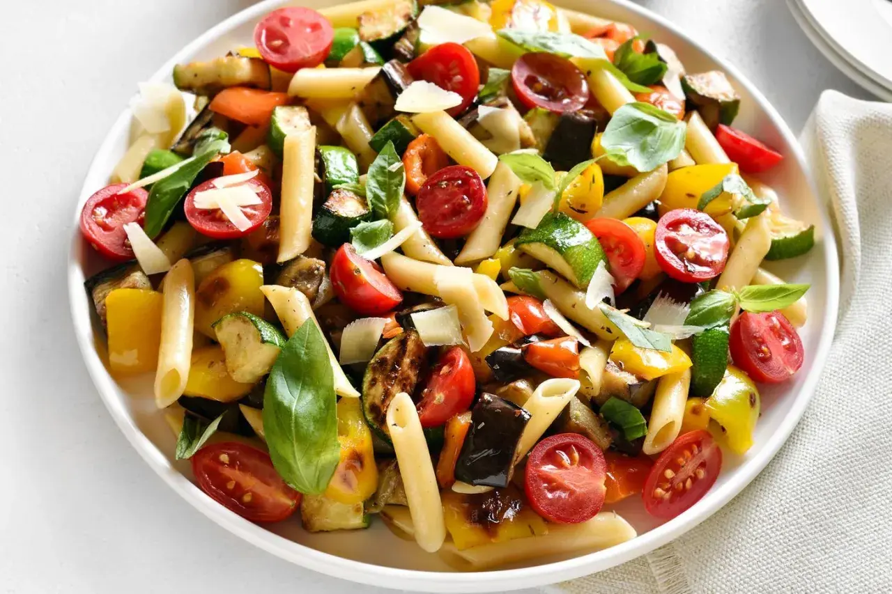 Bunter Nudelsalat ohne Mayo mit Penne, gegrilltem Gemüse wie Zucchini, Aubergine, Paprika, Kirschtomaten und frischem Basilikum, garniert mit Parmesan.