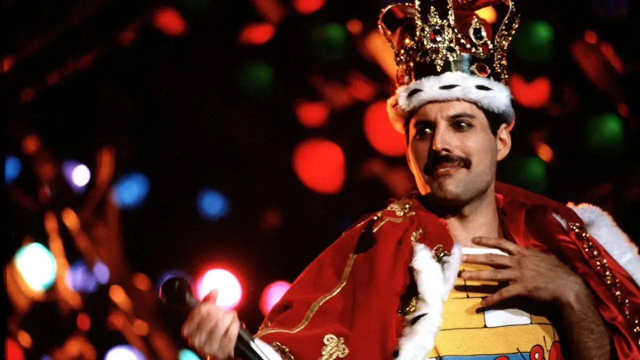 Freddie Mercury w koronie i czerwonym płaszczu, śpiewający swoje legendarne piosenki.