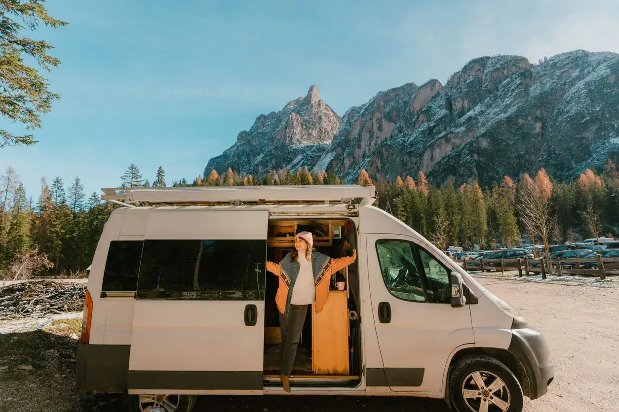 Une femme sort de son fourgon aménagé, profitant d'une vue spectaculaire sur les montagnes. Une image qui pourrait bientôt devenir un souvenir, car les fourgons aménagés vont être interdits.