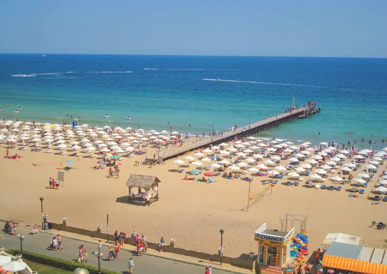 Słoneczny Brzeg, Bułgaria: plaża pełna białych parasoli, molo i turystów cieszących się słońcem i morzem.