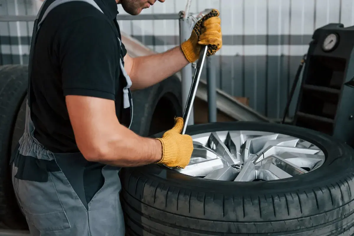 Mechanik w żółtych rękawiczkach używa klucza do opony, pokazując, jak ściągnąć oponę z felgi domowym sposobem.