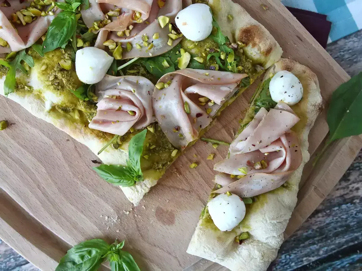 En läcker pinsa pesto med mortadella, mozzarella, pistagenötter och färsk basilika på en träskärbräda.