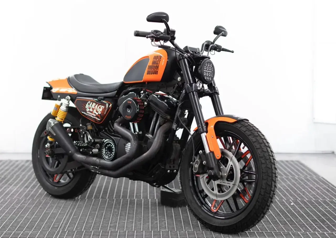 Harley Davidson custom con sella nera, serbatoio arancione e dettagli "Garage". Motore potente e ruote personalizzate.