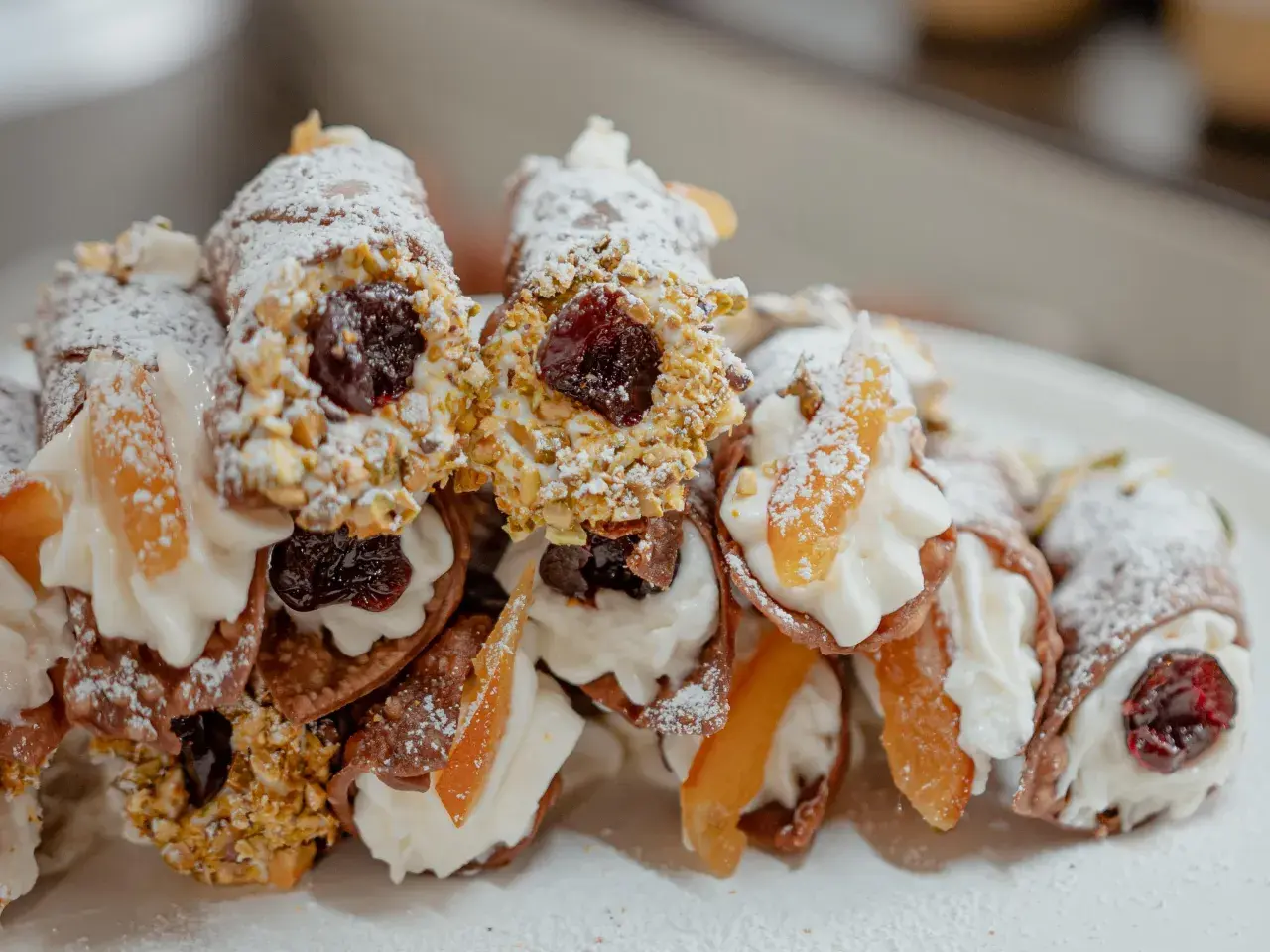 Cannoli garnis avec une généreuse crème de ricotta, des pistaches concassées, des cerises confites et des fruits confits. Saupoudrés de sucre glace.