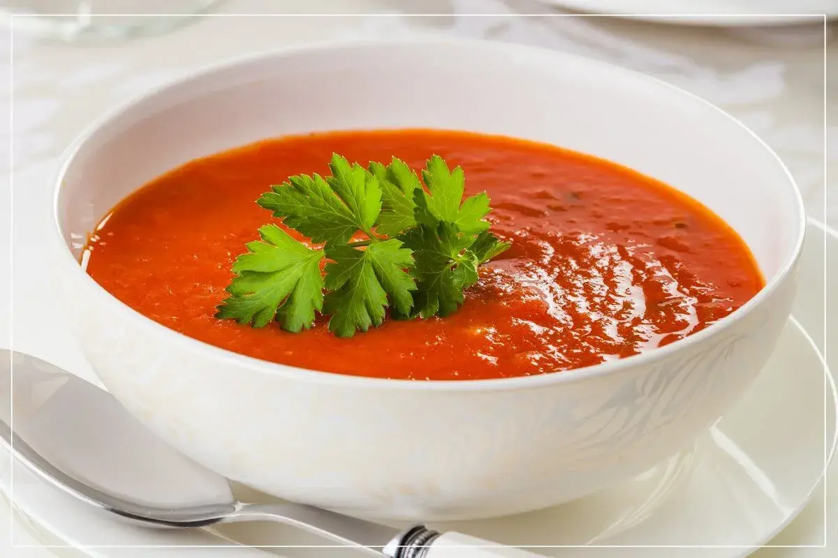 Eine Schüssel cremiger Tomatensuppe mit Petersilie garniert, daneben ein Löffel.