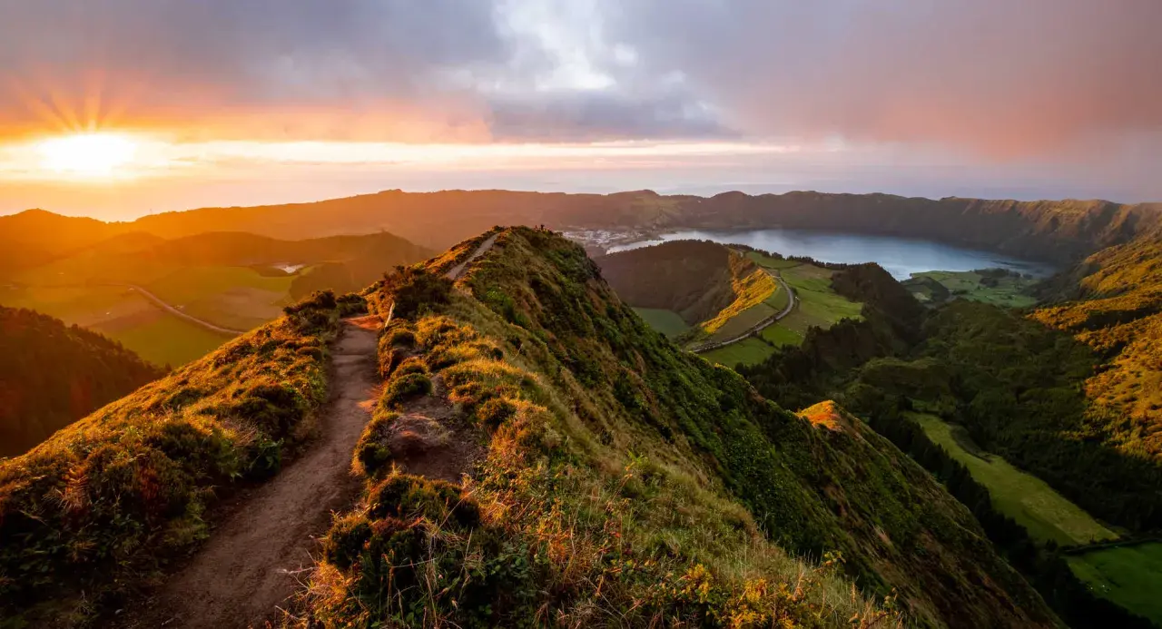 Magnifique paysage des Açores au coucher du soleil, avec un sentier serpentant sur une crête verdoyante menant à un lac paisible.