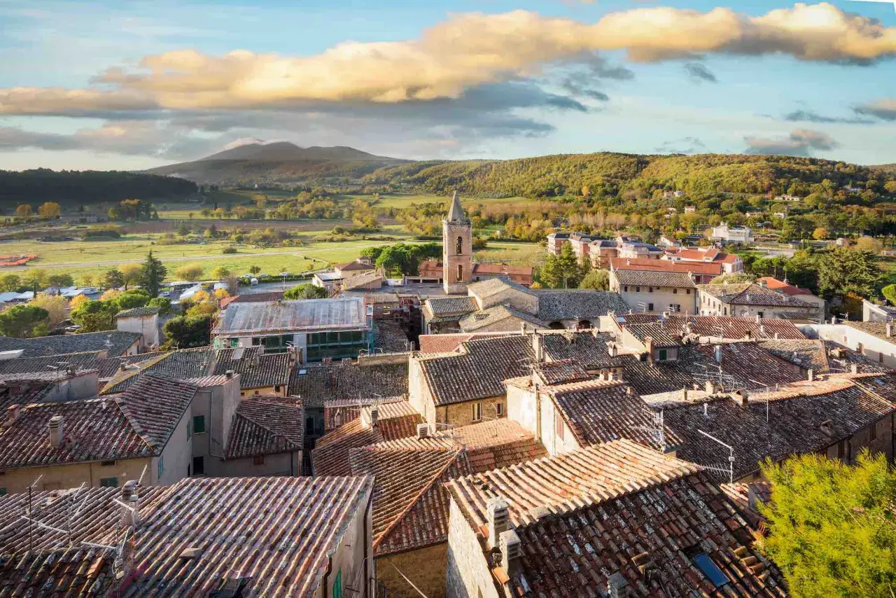 Panoramica di Sarteano cosa vedere: tetti in cotto, campanile e colline verdi sotto un cielo nuvoloso.