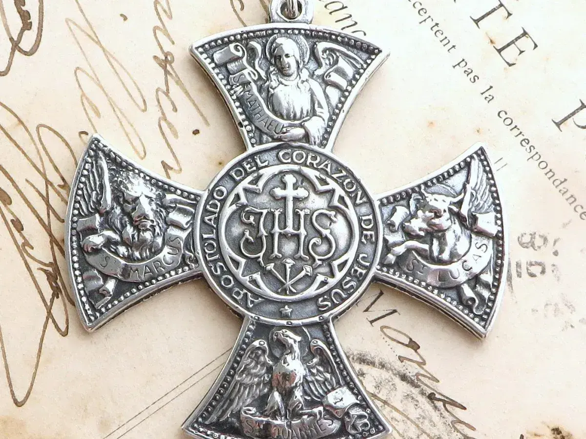 Srebrny medalion z symbolem IHS i symbolami ewangelistów: lew (św. Marek), anioł (św. Mateusz), wół (św. Łukasz) i orzeł (św. Jan).