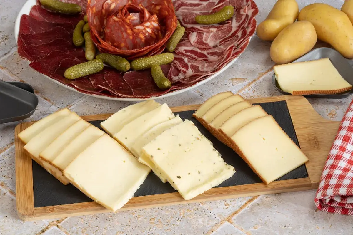 Plateau de charcuterie et fromages variés, prêts pour une recette fromage à raclette. Pommes de terre et cornichons complètent ce festin.