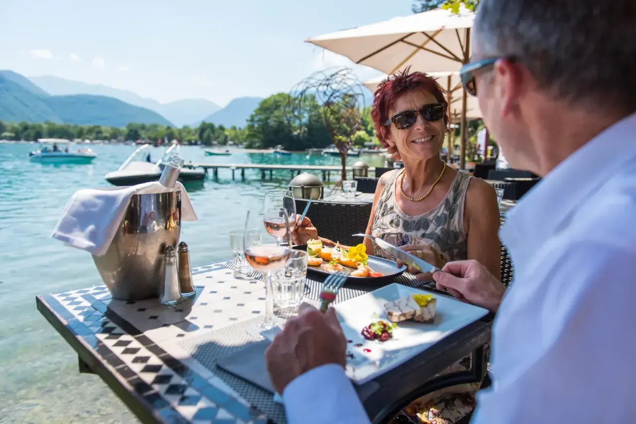 Un couple savoure un repas gastronomique avec vue sur le lac d'Annecy. La plage est magnifique.
