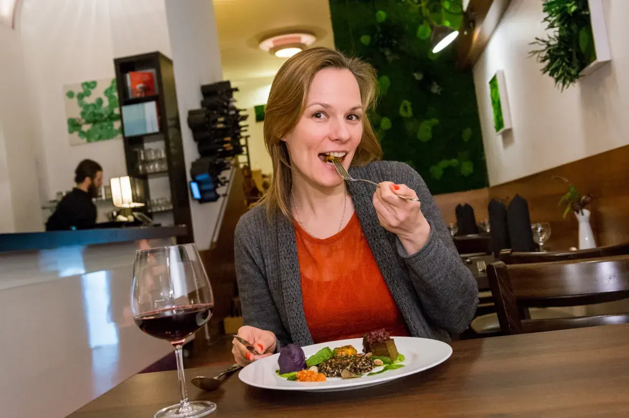 Frau genießt ein veganes Gericht in einem Berliner Restaurant. Auf dem Teller sind bunte Komponenten und ein Glas Rotwein.