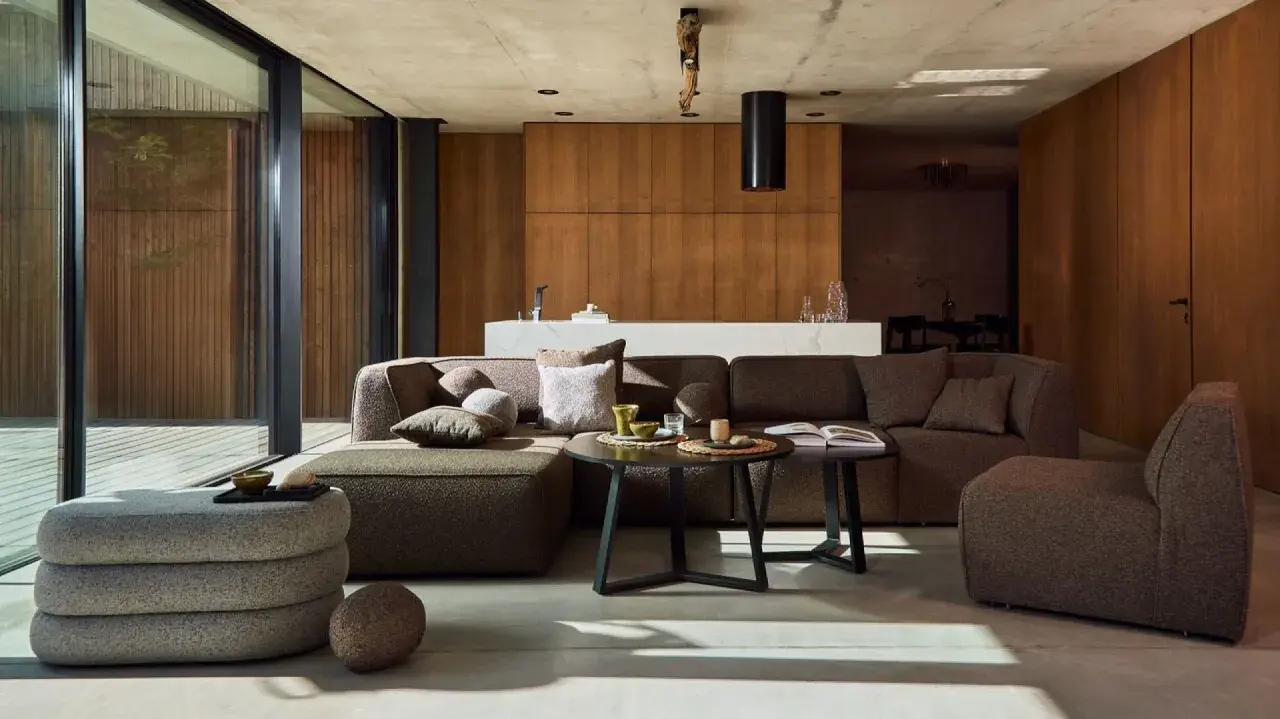 Nowoczesny salon w stylu bauhaus z dużą, narożną sofą, drewnianymi panelami i betonowym sufitem.