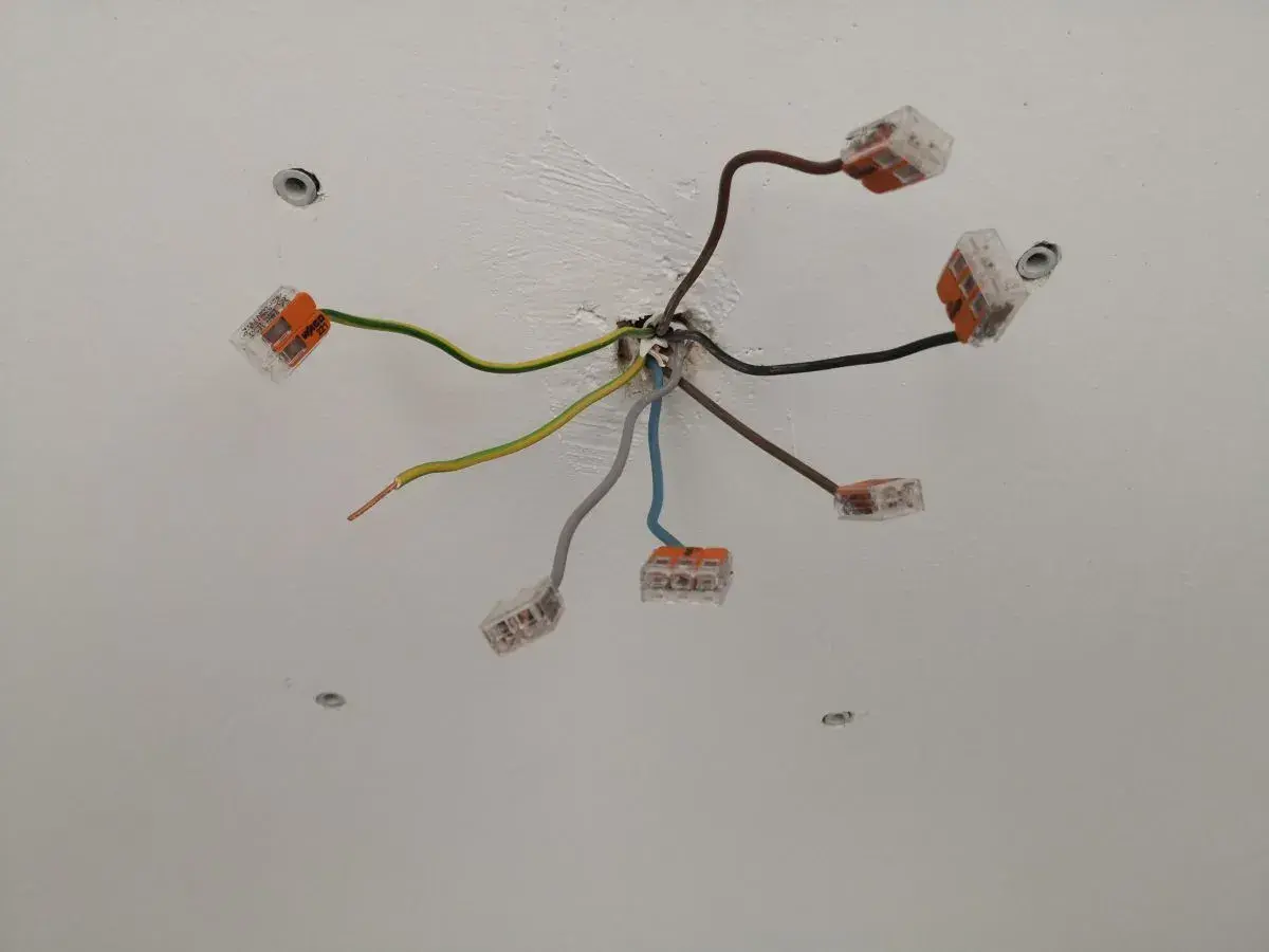 Sufit z instalacją elektryczną. Widać kilka przewodów, w tym czarny kabel elektryczny, połączonych złączkami.