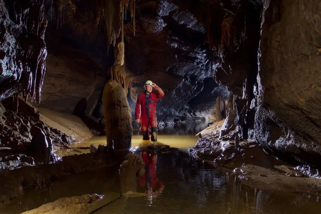 Eksplorator w jaskini, zanurzony po kolana w wodzie, odkrywa tajemnice speleologii.