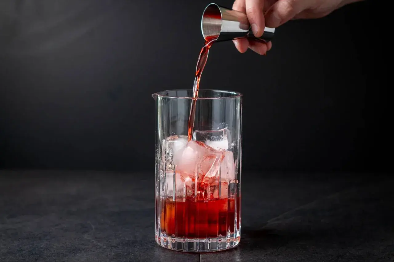 Ein Barkeeper gießt rote Flüssigkeit in ein Glas mit Eiswürfeln. Der klassische Cocktail Negroni nimmt Gestalt an.