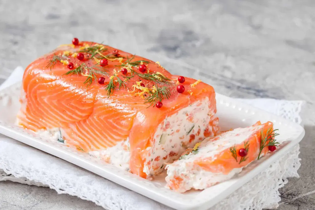 Une délicieuse terrine de saumon, garnie d'aneth, de baies roses et de zeste de citron, prête à être dégustée.