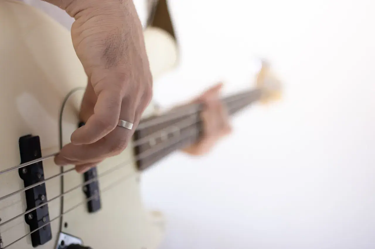 Dłoń z pierścionkiem ćwiczy naukę gry na gitarze basowej, szarpiąc struny.