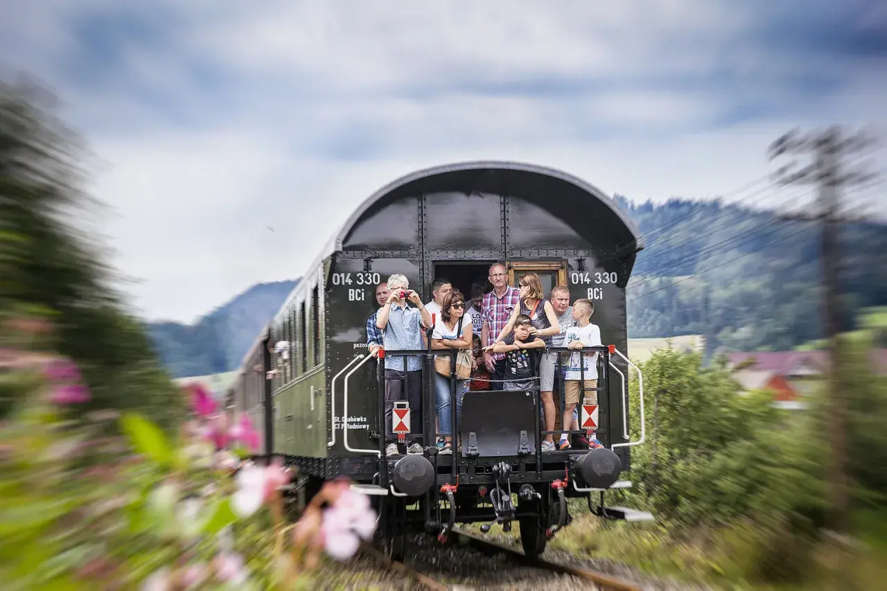Familie genießt die Fahrt von Dresden nach Polen im offenen Waggon eines historischen Zuges, umgeben von grüner Natur.