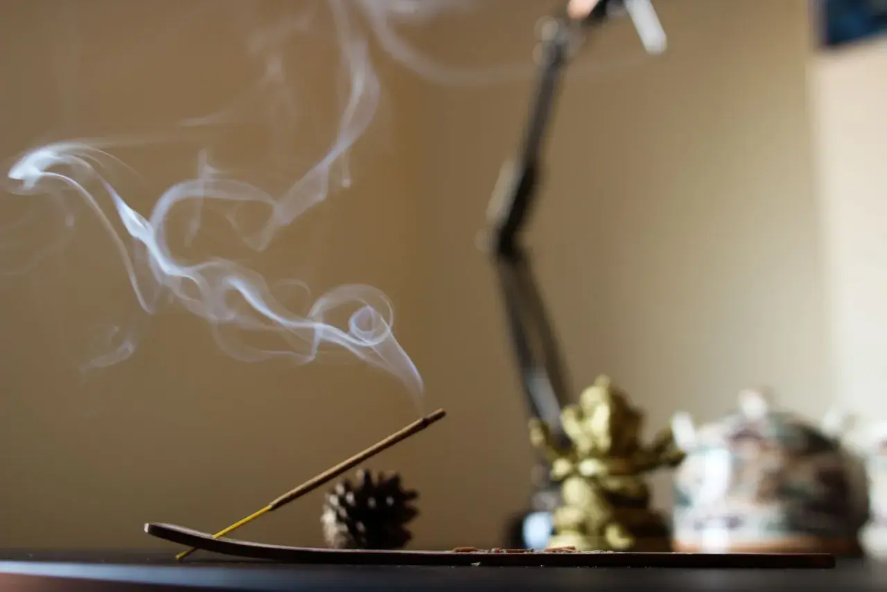 El humo del incienso se eleva en espirales blancas, creando un ambiente sereno junto a una figura dorada y una tetera decorada.