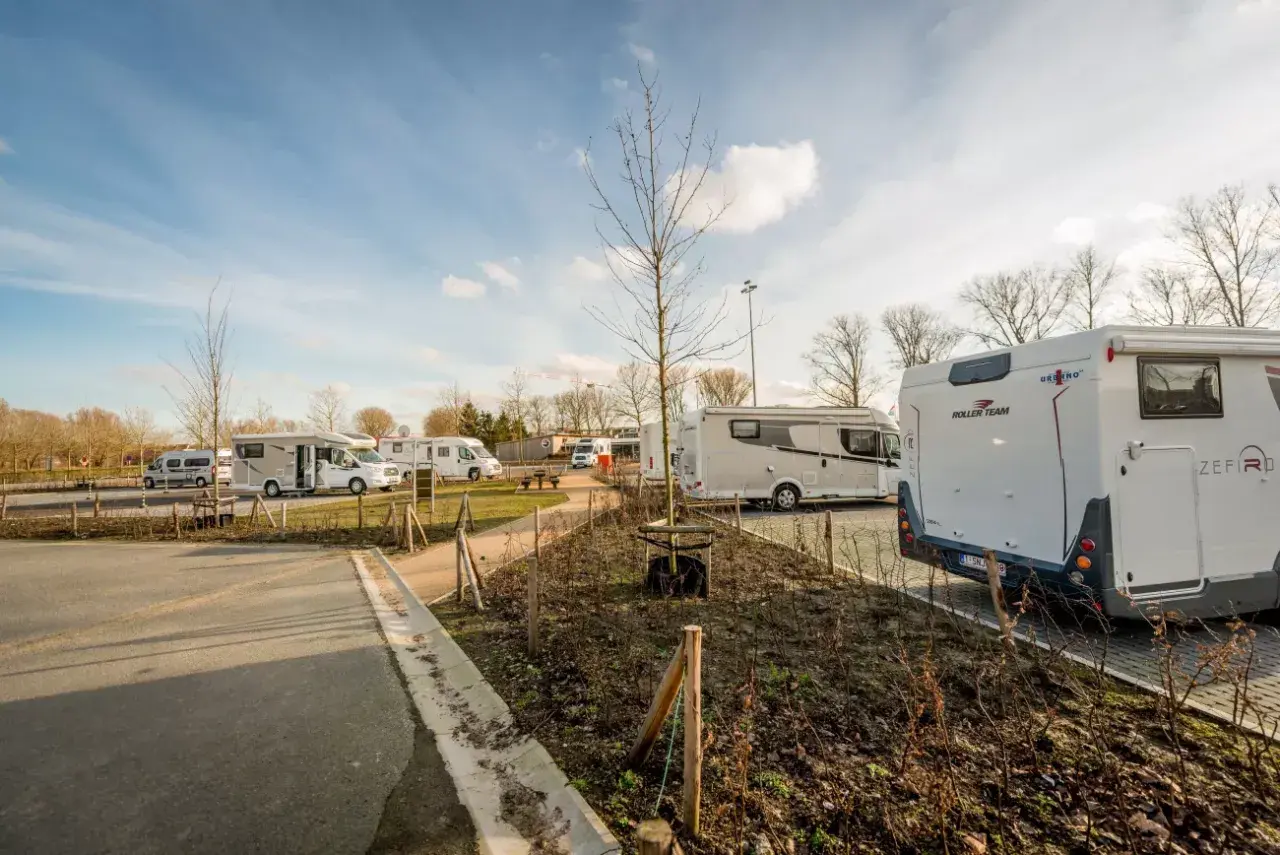 Vue d'une aire camping car Bruges avec plusieurs véhicules stationnés sous un ciel bleu.