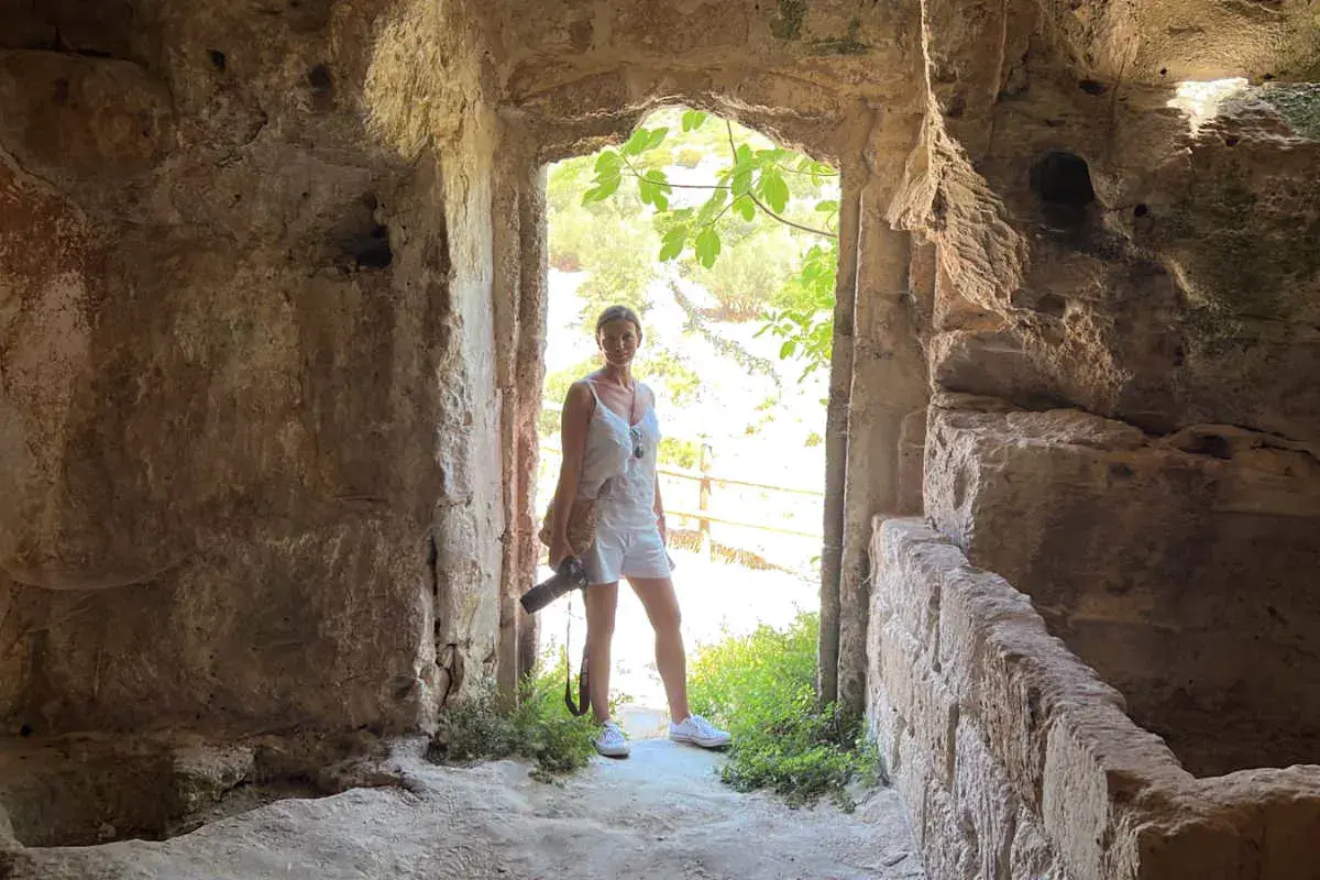 Una donna in abito bianco, con una macchina fotografica in mano, esplora antiche rovine. Un momento di travel photography.