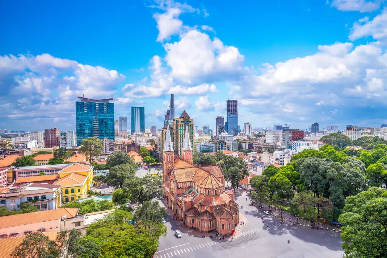 Piękna pogoda w Ho Chi Minh: katedra Notre Dame i nowoczesne wieżowce na tle błękitnego nieba z chmurami.