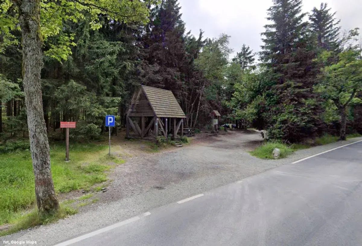 Drewniana wiata i parking przy leśnej drodze. To miejsce to Lisia Przełęcz, idealne na odpoczynek w otoczeniu drzew.