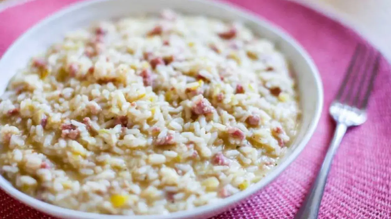 Un cremoso risotto salsiccia, con trocitos de salchicha italiana, servido en un cuenco blanco sobre un mantel rosa.